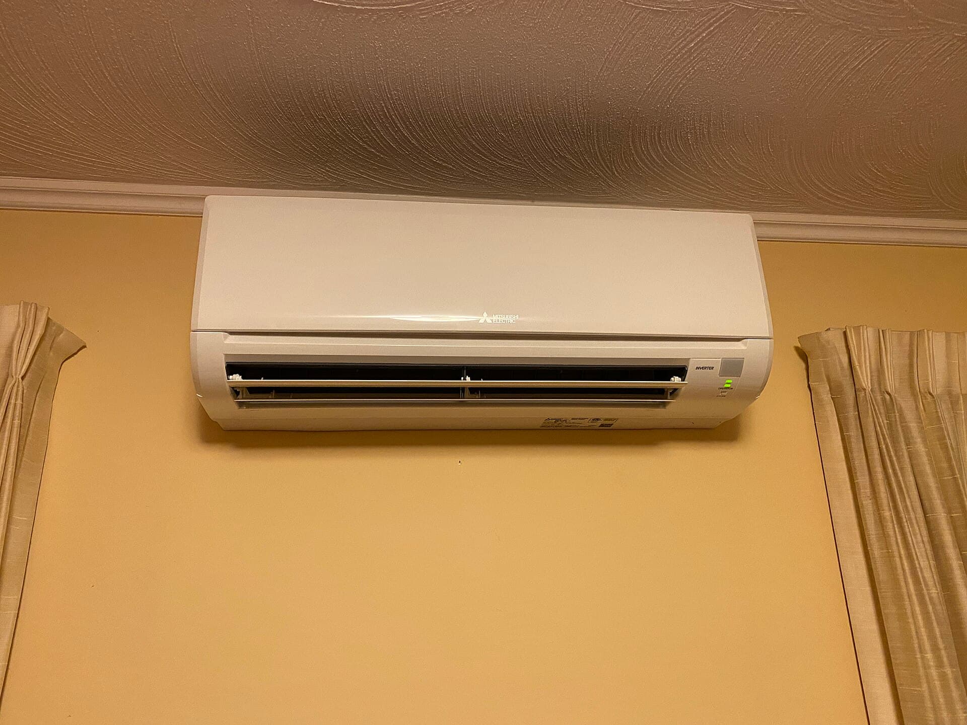 Mitsubishi ductless mini-split indoor unit mounted high on a home's wall — the quiet head unit each room gets